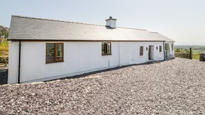 A single-story white building with a sloped roof, a chimney, and a gravel driveway. - Pen Y Braich Uchaf (Garndolbenmaen)