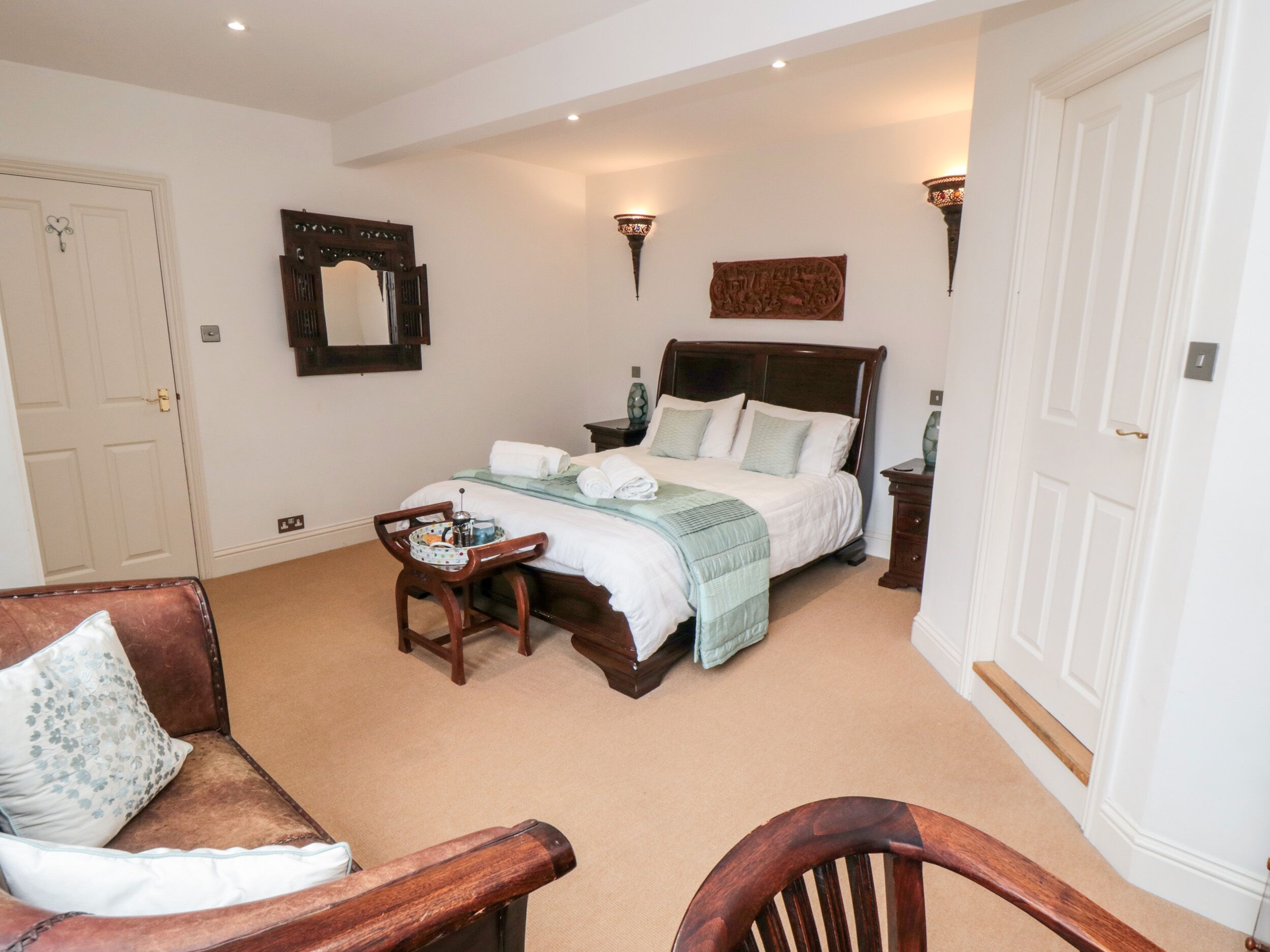 A bedroom with a large bed, bedside tables, a chair, and a mirror on the wall.