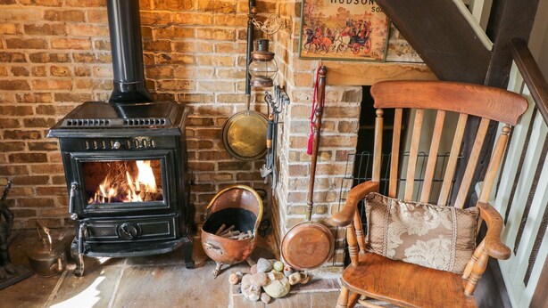 A rustic room with a brick wall, a black wood-burning stove, a wooden chair, and a sign reading "HUDSON SO." - Old Stables Cottage (Saltburn-by-the-Sea)
