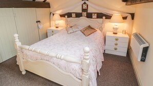 A bedroom with a four-poster bed, two bedside tables with lamps, a radiator, and a wooden ceiling. - Old Stables Cottage (Saltburn-by-the-Sea)