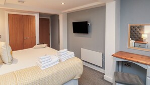 Una camera da letto con un letto, una TV fissata al muro, un comodino con una lampada e una porta in legno.