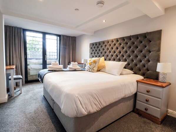 A hotel room with a large bed, a bedside table with a lamp, a chair, and a view of the outdoors through a window. - Blue Peter @ Engine Shed (Whitby)