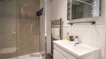 A modern bathroom with a glass shower enclosure, a white sink with a mirror, and a towel rack.