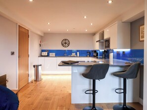 A modern kitchen with a central island, bar stools, and a clock on the wall. - Blue Peter @ Engine Shed (Whitby)