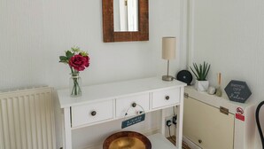 Un tocador blanco con espejo de madera, un florero con flores, una lámpara y un letrero que dice "ON THE LOVE TO BE BESIDE THE SEASIDE".