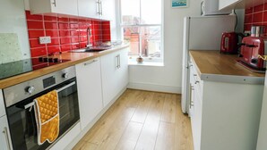 Una cocina con armarios blancos, salpicadero rojo, ventana con persiana roja, microondas, tostadora y hervidor.