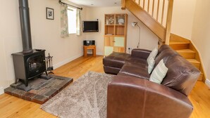 A living room with a fireplace, a leather sofa, a TV, and a staircase. - The Dairy (Tarporley)