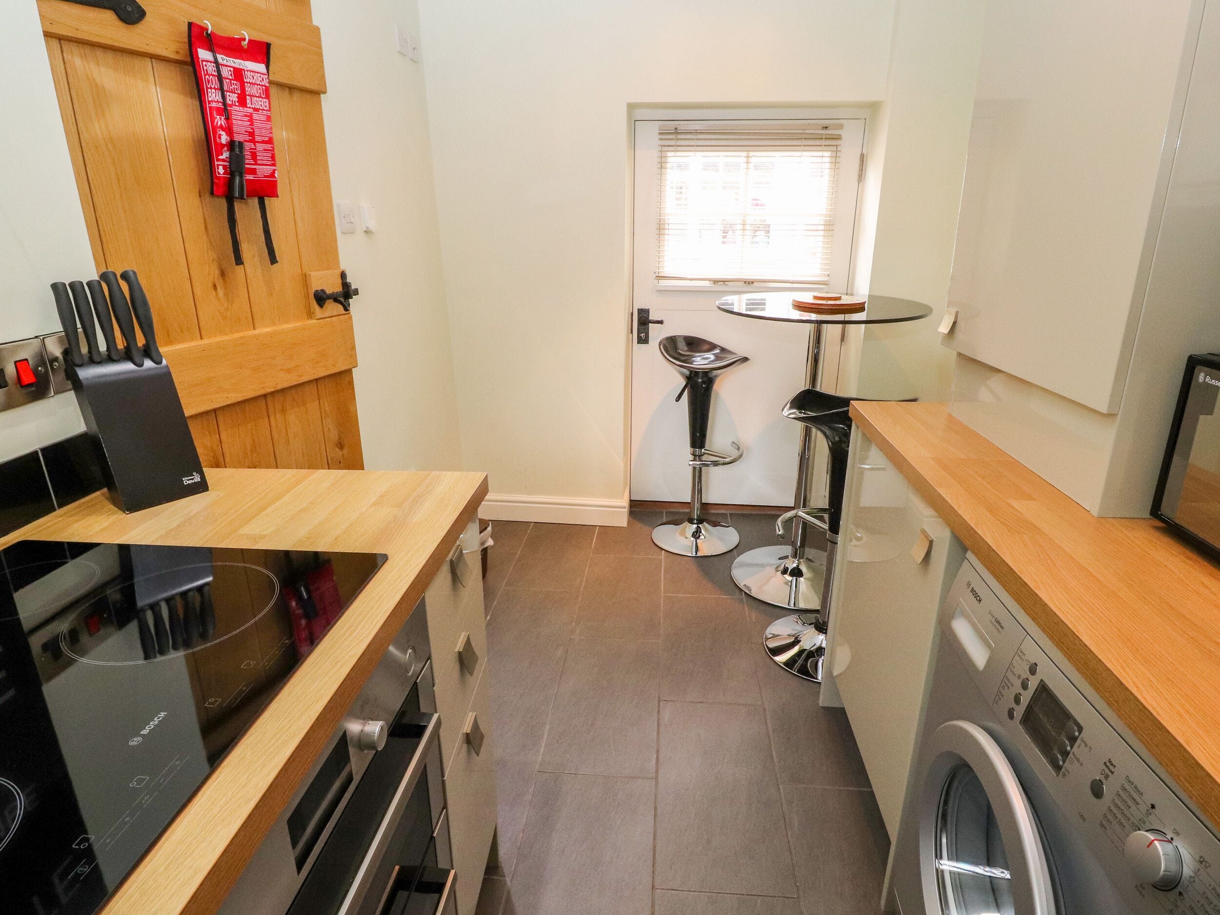 A compact kitchen with a Bosch oven, a washing machine, and a small dining area with a table and two stools.