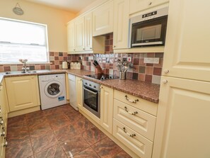 A compact kitchen with a washing machine, oven, microwave, and a tiled backsplash. - Gowanlea (Hexham)