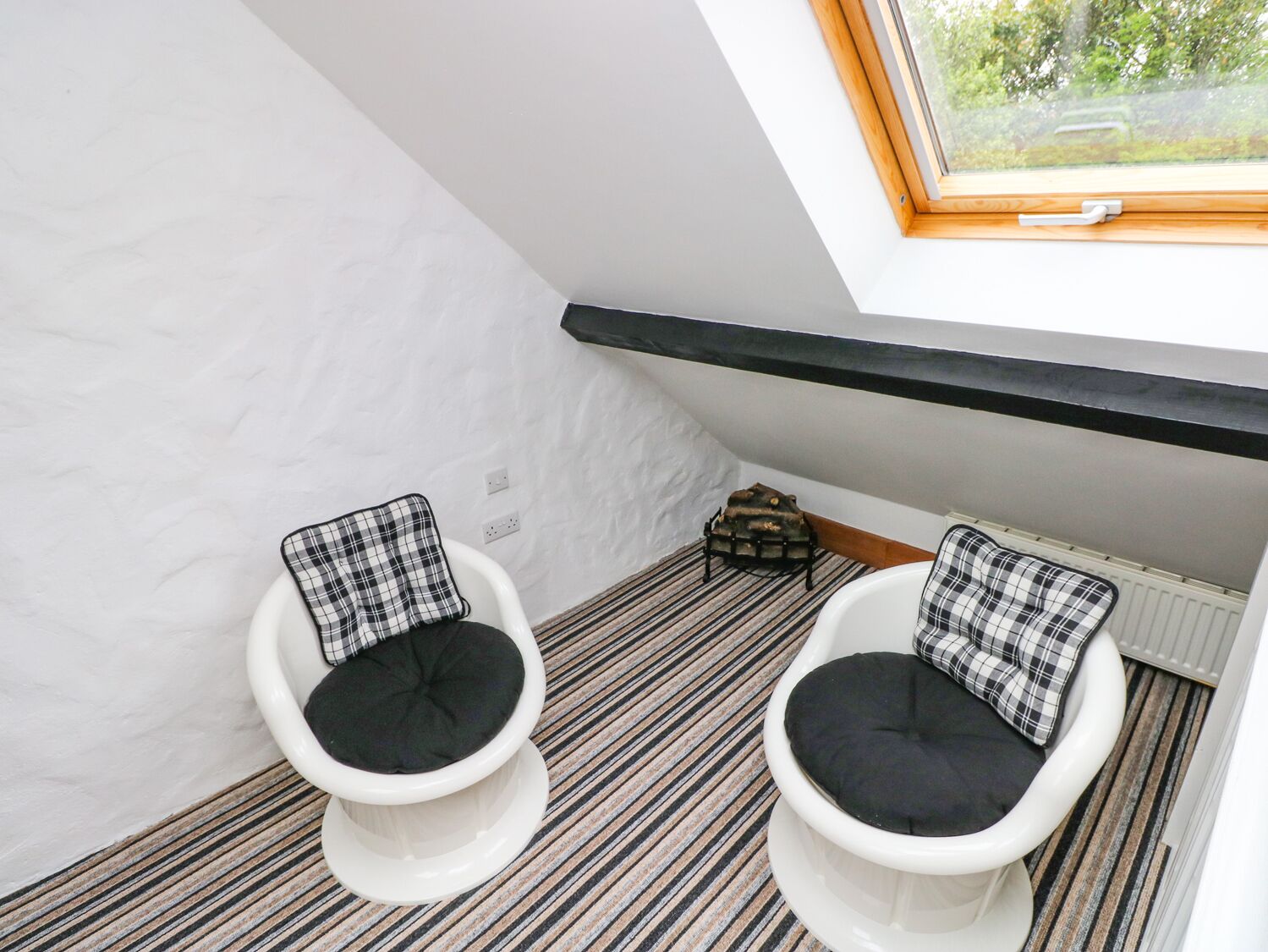 A small, modern bathroom with two white toilets, black cushioned seats, a striped floor, and a skylight.