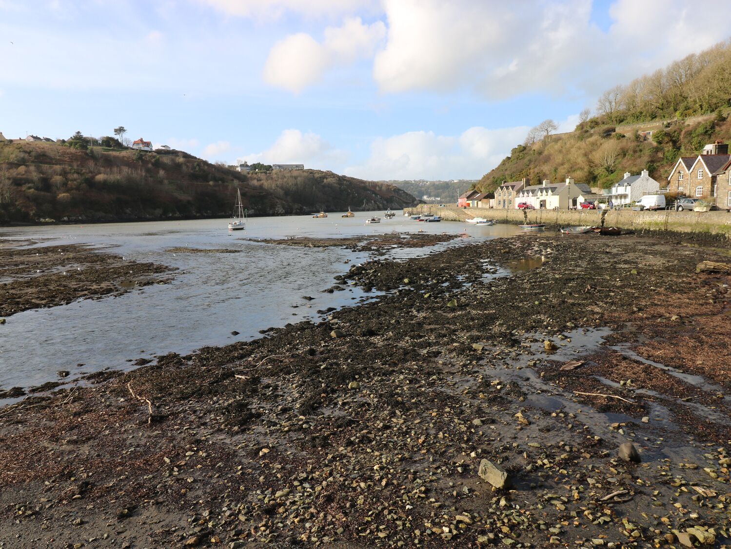 Une zone côtière caractérisée par un rivage rocheux, la présence de bateaux et de maisons le long du bord de l’eau.
