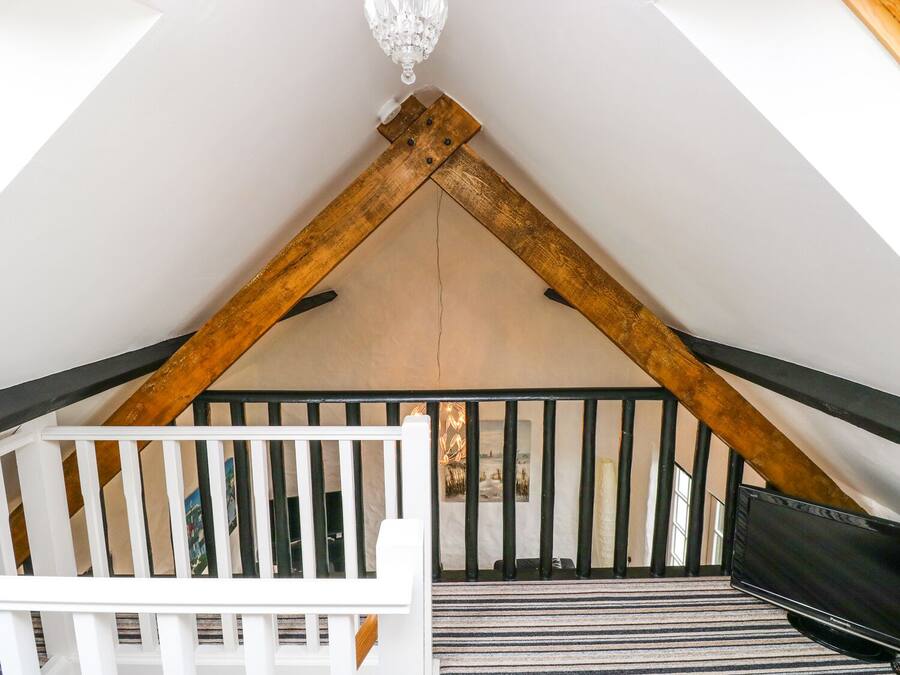 A room with a sloped ceiling, wooden beams, a white crib, a black TV, and a striped carpet.