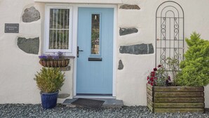 A house with a blue door, stone walls, a nameplate, a window with bars, a metal gate, and potted plants.
