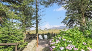 A stone pathway leading to a seating area with white chairs, surrounded by lush greenery and flowering plants.