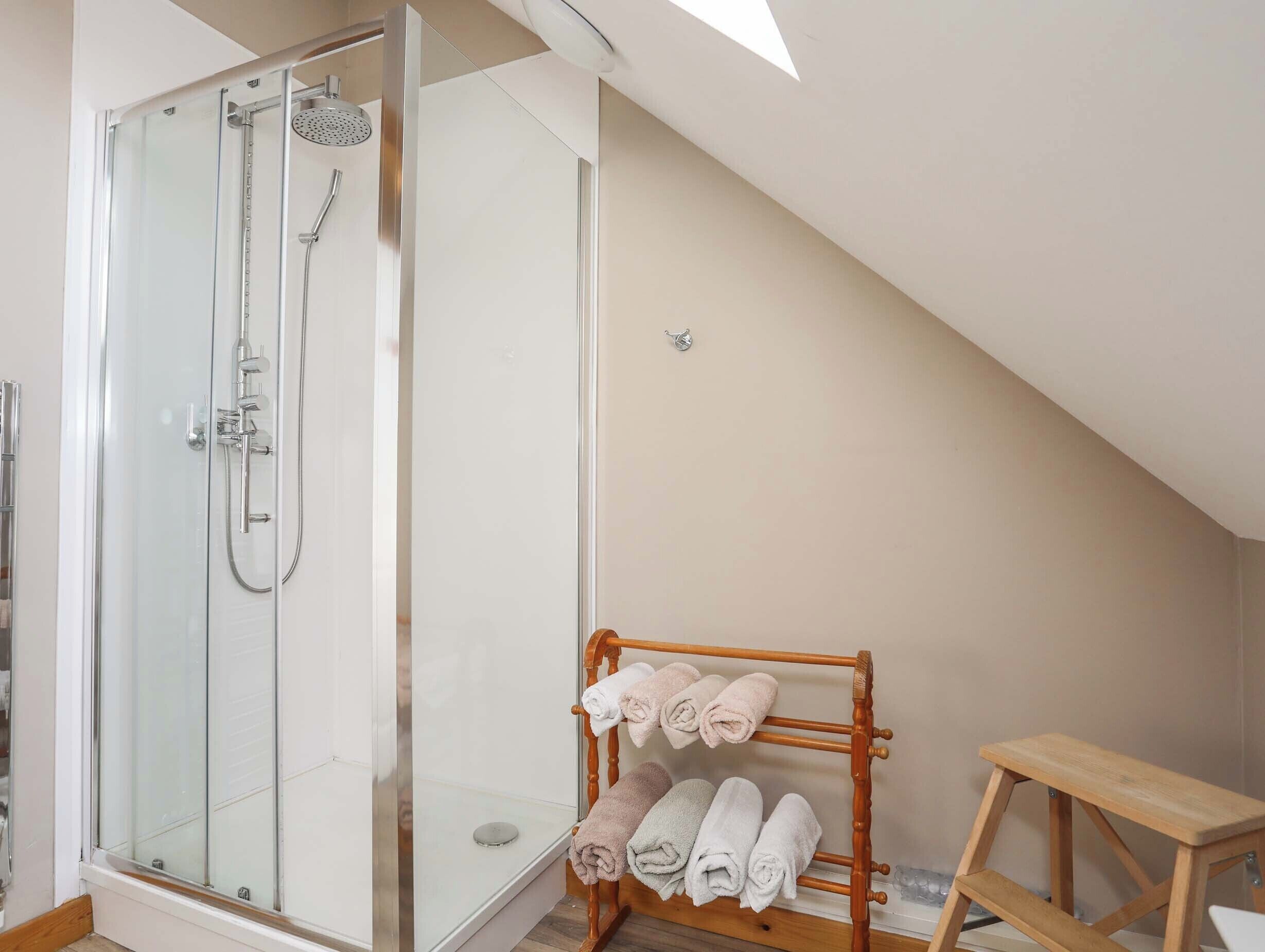 Un baño moderno con ducha acristalada, un perchero de madera y un taburete de madera.