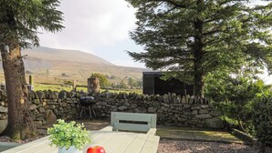 A wooden table with two potted plants and two apples, a stone wall, and a stone bench.