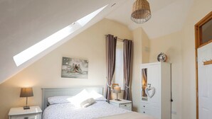 A bedroom with a sloped ceiling, a bed with a white headboard, a bedside table with a lamp, a wardrobe, and a painting on the wall.
