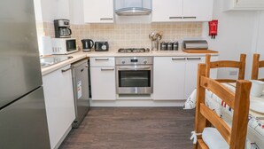 Une cuisine moderne avec des meubles blancs, un réfrigérateur en acier inoxydable, un four à micro-ondes, une machine à café et une cuisinière à gaz.