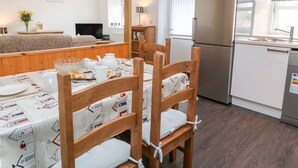 Une cuisine moderne dotée d’un réfrigérateur encastré, d’une table à manger en bois avec des chaises, et d’un coin salon confortable avec un canapé et un téléviseur.