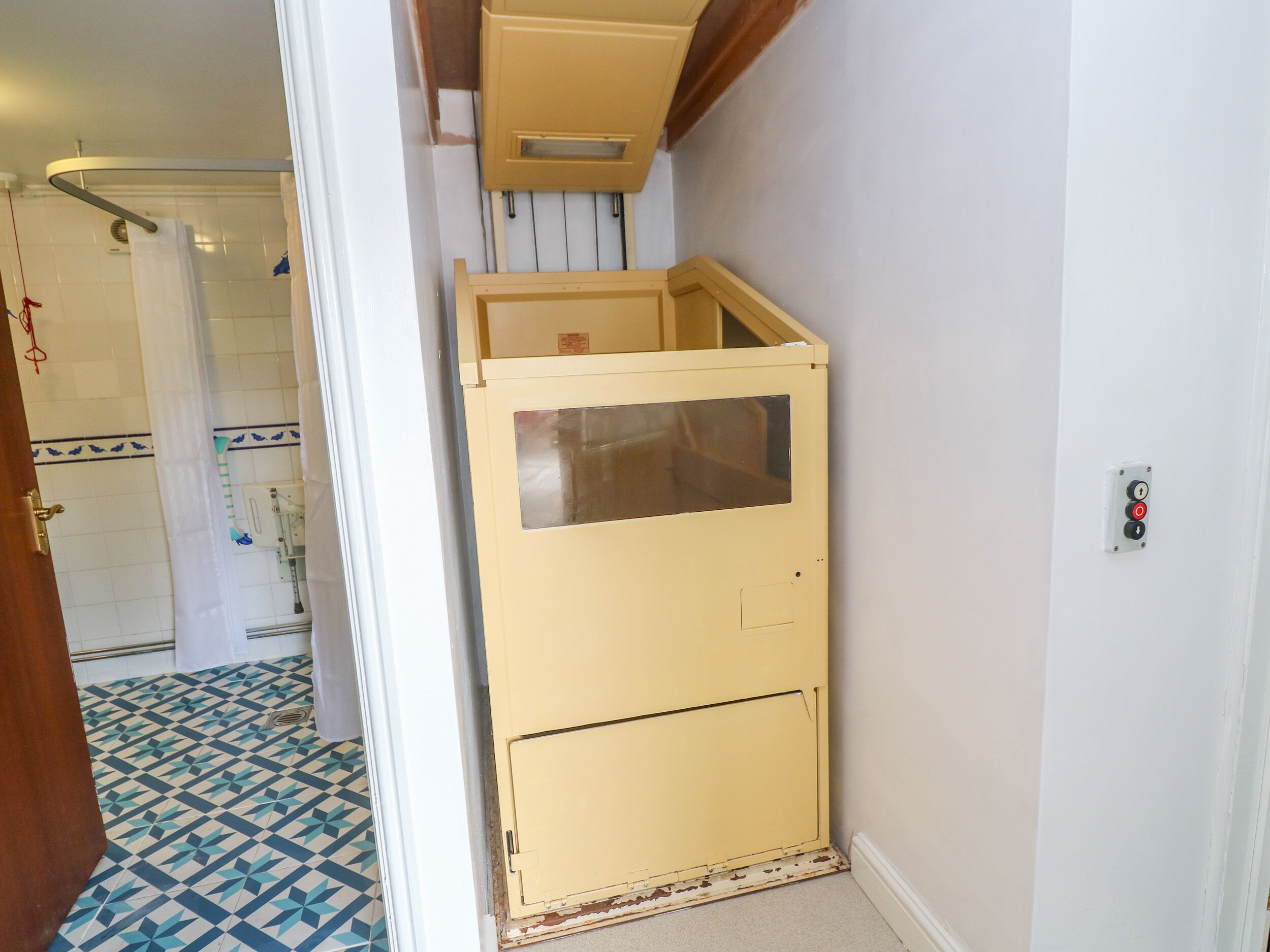 Un pasillo estrecho con un armario beige, suelo de baldosas y una puerta que da a un baño.