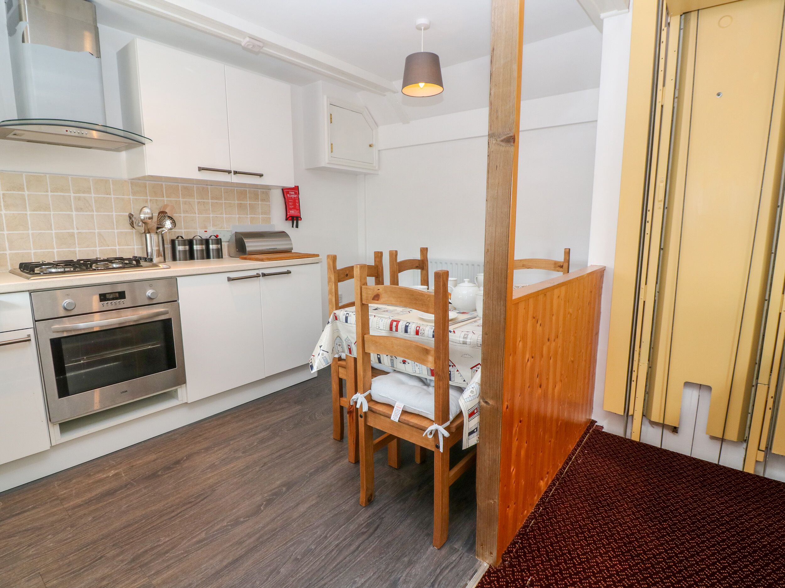 A compact kitchen with white cabinets, a gas stove, an oven, and a wooden dining table with chairs.