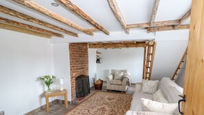 Un salon chaleureux avec des poutres apparentes, une cheminée en briques, un canapé confortable et un tapis à motifs.