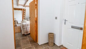 Un couloir avec une porte blanche, un panier en osier et un lit recouvert d’une couverture à carreaux.