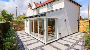 Une maison moderne dotée d’une extension en verre, d’une terrasse carrelée et d’un toit recouvert de tuiles rouges.