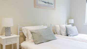 A bedroom with two beds, white bedding, striped pillows, a bedside table with a lamp, and a framed picture on the wall.