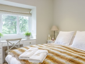 Quarto com cama, janela com vista para árvores, escrivaninha e cadeira.