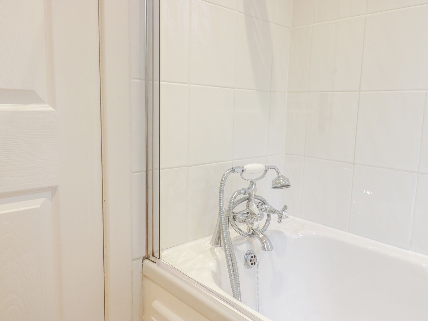 A bathroom with a white bathtub, a glass shower enclosure, and white tiled walls.