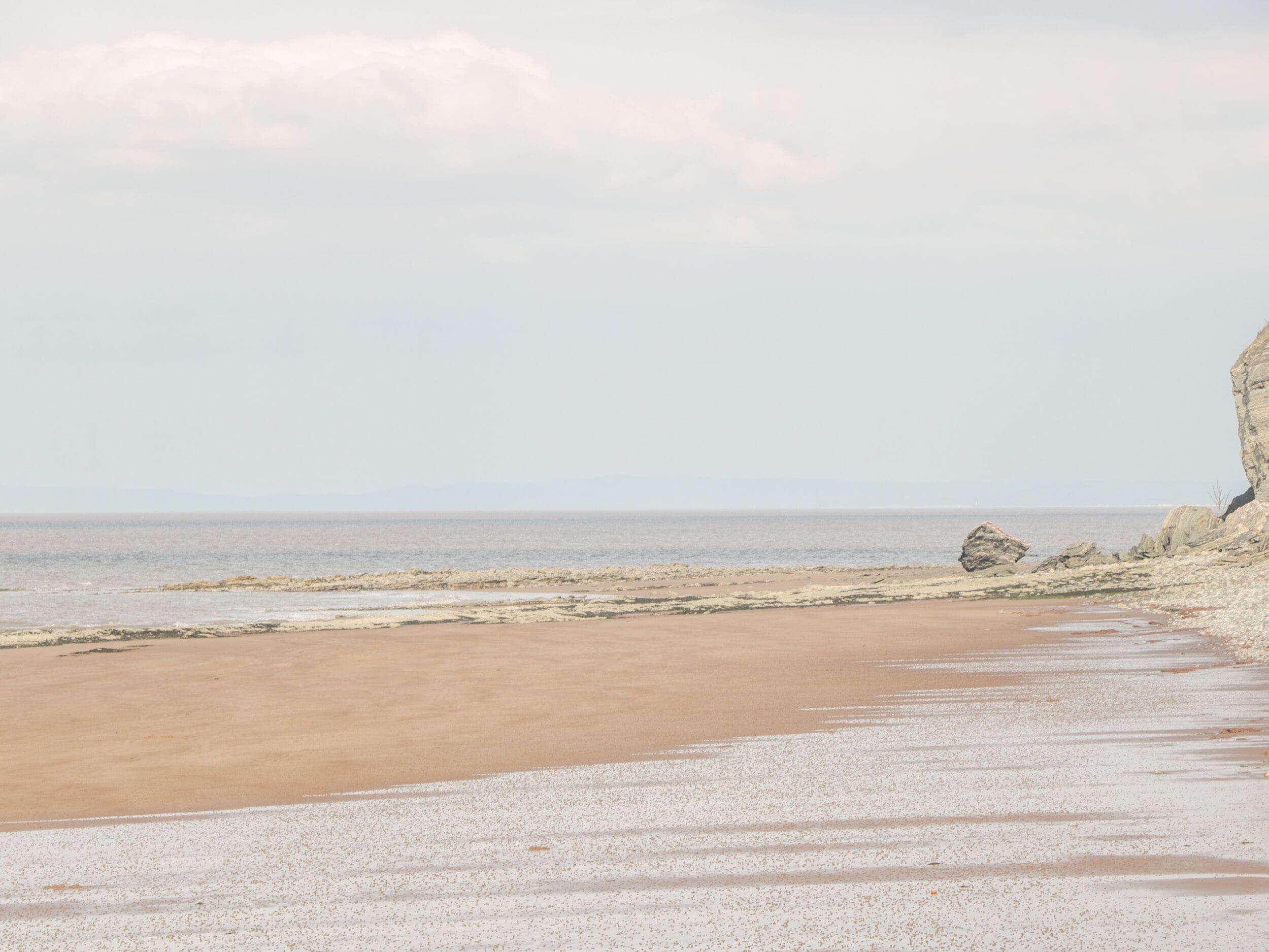 A beach with a rocky cliff and calm sea.