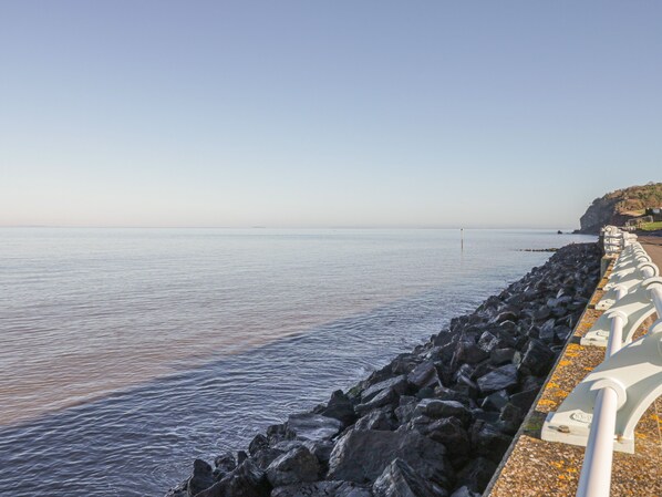 A coastal walkway with a rocky barrier and a clear view of the sea. - 7 Malt House Court (Watchet)