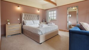 A bedroom with a large bed, a dresser, a mirror, and a blue armchair. - Manor Cottage (Northallerton)