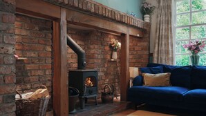 A cozy living room with a brick fireplace, a blue sofa, and a window with curtains. - Manor Cottage (Northallerton)