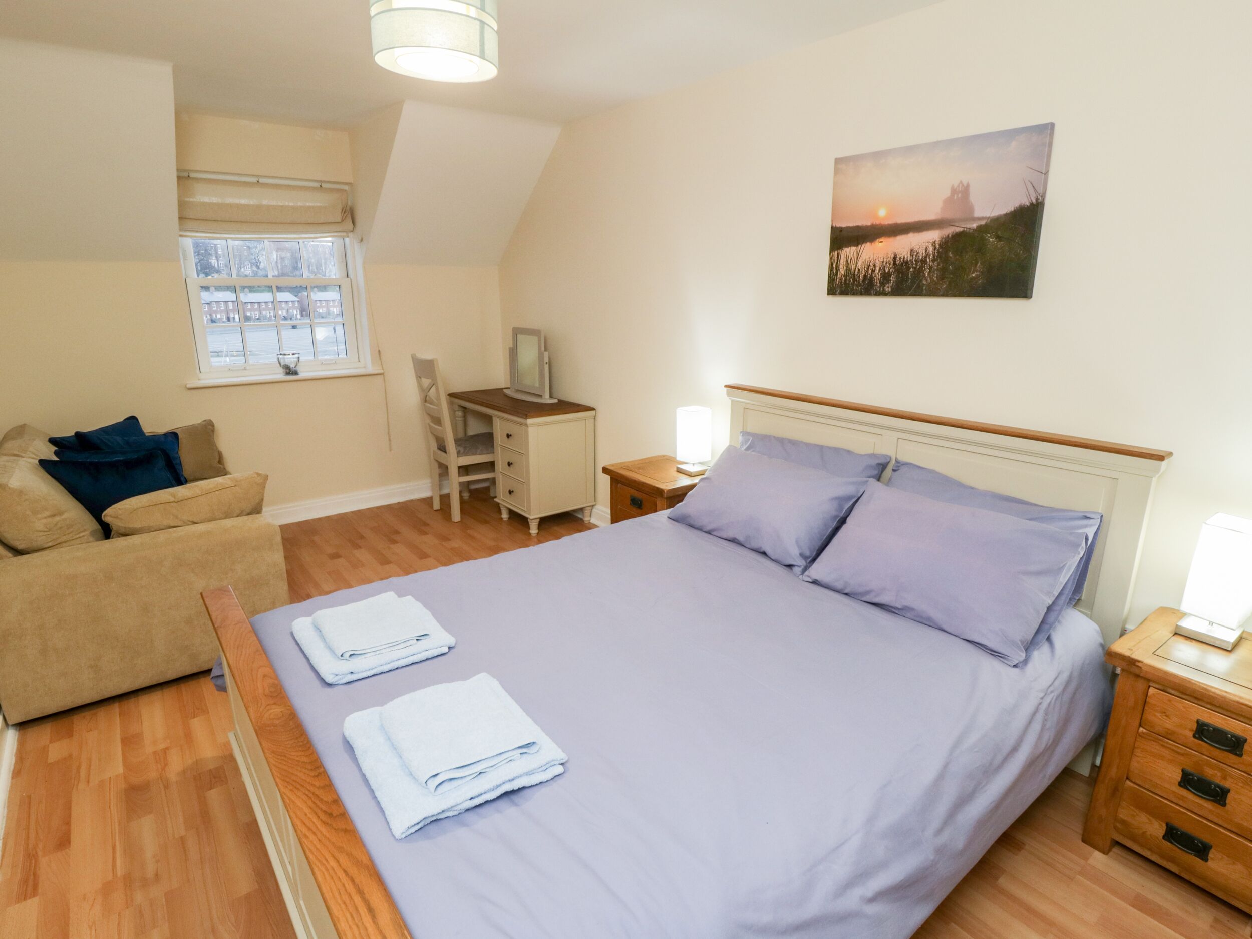 Une chambre à coucher avec un lit, un bureau, une chaise, une fenêtre et un tableau accroché au mur.