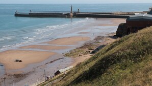 A coastal beach with a lighthouse, a pier, and a building with a sloped roof.