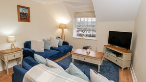 A cozy living room with a blue sofa set, a flat-screen TV, a lamp, and a window with a view of boats.