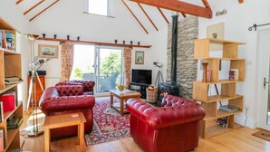 A cozy living room with a fireplace, leather sofas, wooden flooring, and a stone wall. - The Barn at Waen y Ffynnon (Ruthin)