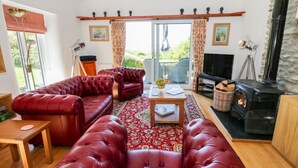 A cozy living room with a red leather sofa set, a wooden coffee table, a fireplace, and a television. - The Barn at Waen y Ffynnon (Ruthin)