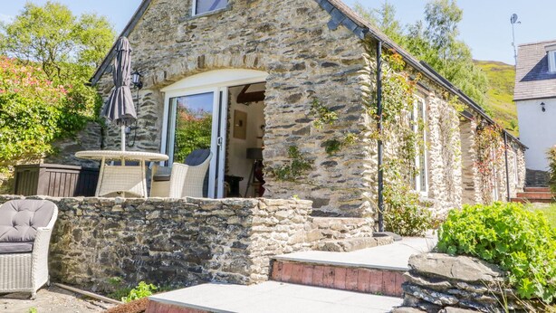 A stone building with a sloped roof, a small window, and a door leading to an interior space. - The Barn at Waen y Ffynnon (Ruthin)