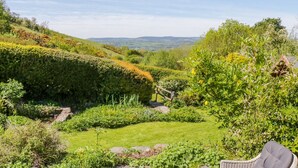 A garden with a grassy area, a stone pathway, and a wicker chair. - The Barn at Waen y Ffynnon (Ruthin)