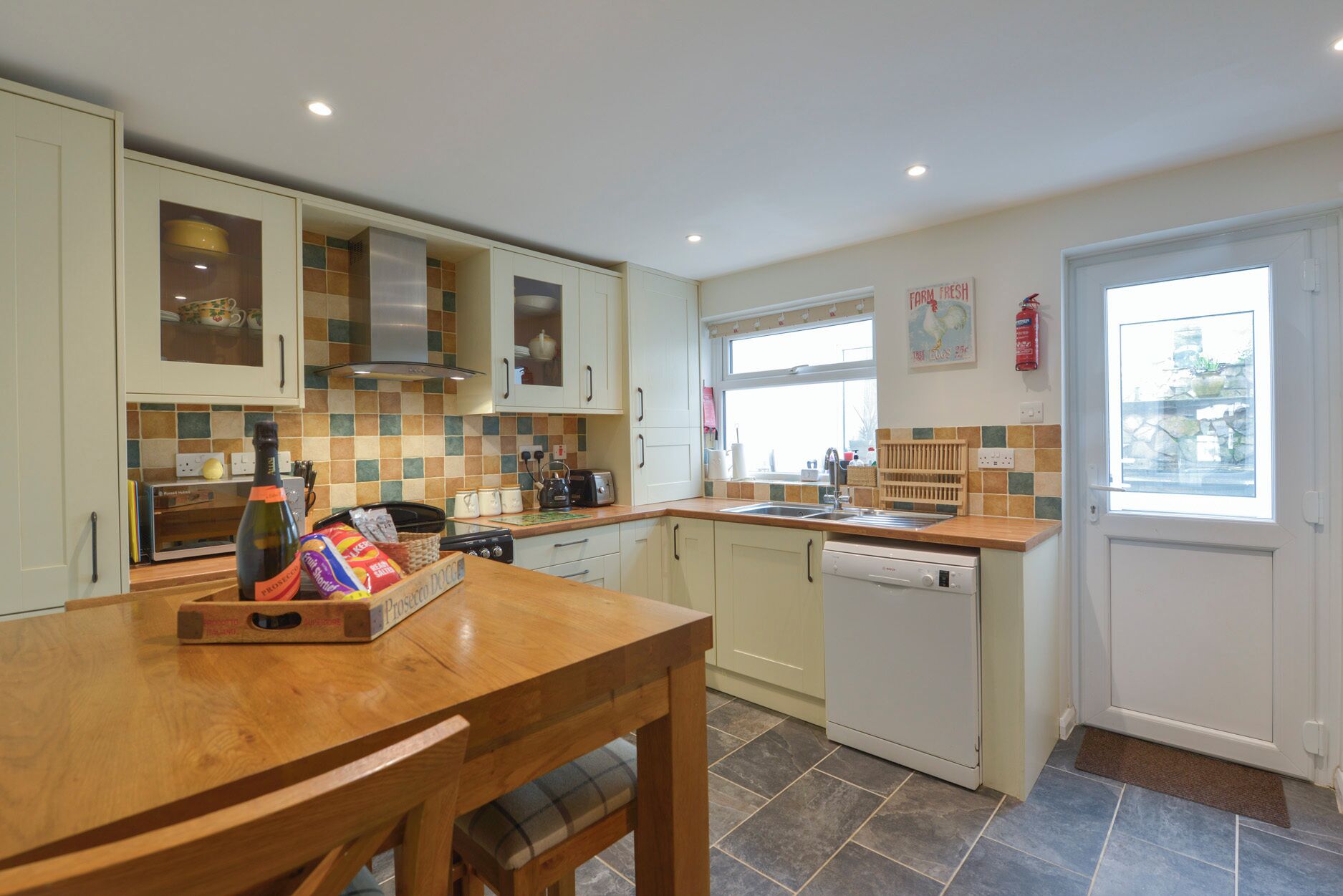 A kitchen with white cabinets, a wooden table, a dishwasher, and a window with a view.