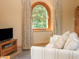 Un soggiorno con televisione su un mobile in legno, un divano con cuscini decorati e una finestra con tende.