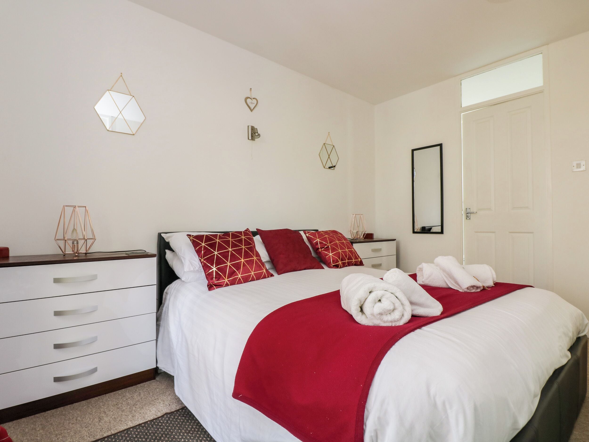 A neatly arranged bedroom with a bed, a dresser, a mirror, and decorative wall hangings.