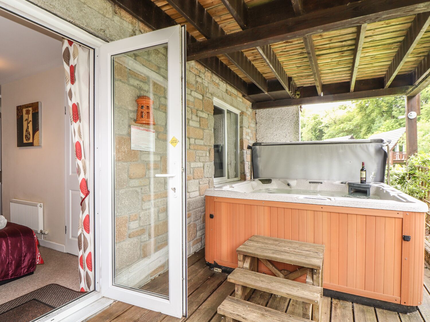 Un jacuzzi con escalones de madera y una terraza de madera, una puerta de cristal y un muro de ladrillo.