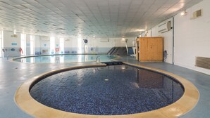 A large indoor swimming pool with tiled floors and walls, surrounded by windows and a wooden structure. - Valley Lodge 52 (Gunnislake)