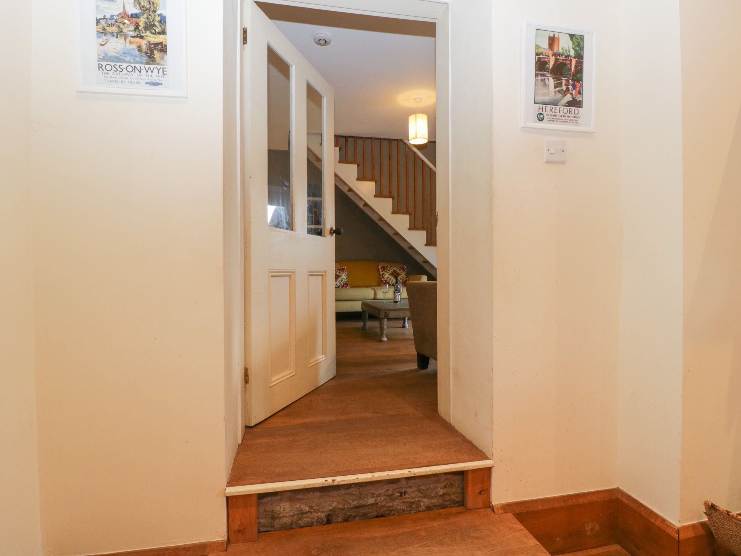 A hallway leading to a staircase with a wooden floor and a door at the end. There are two framed pictures on the walls.