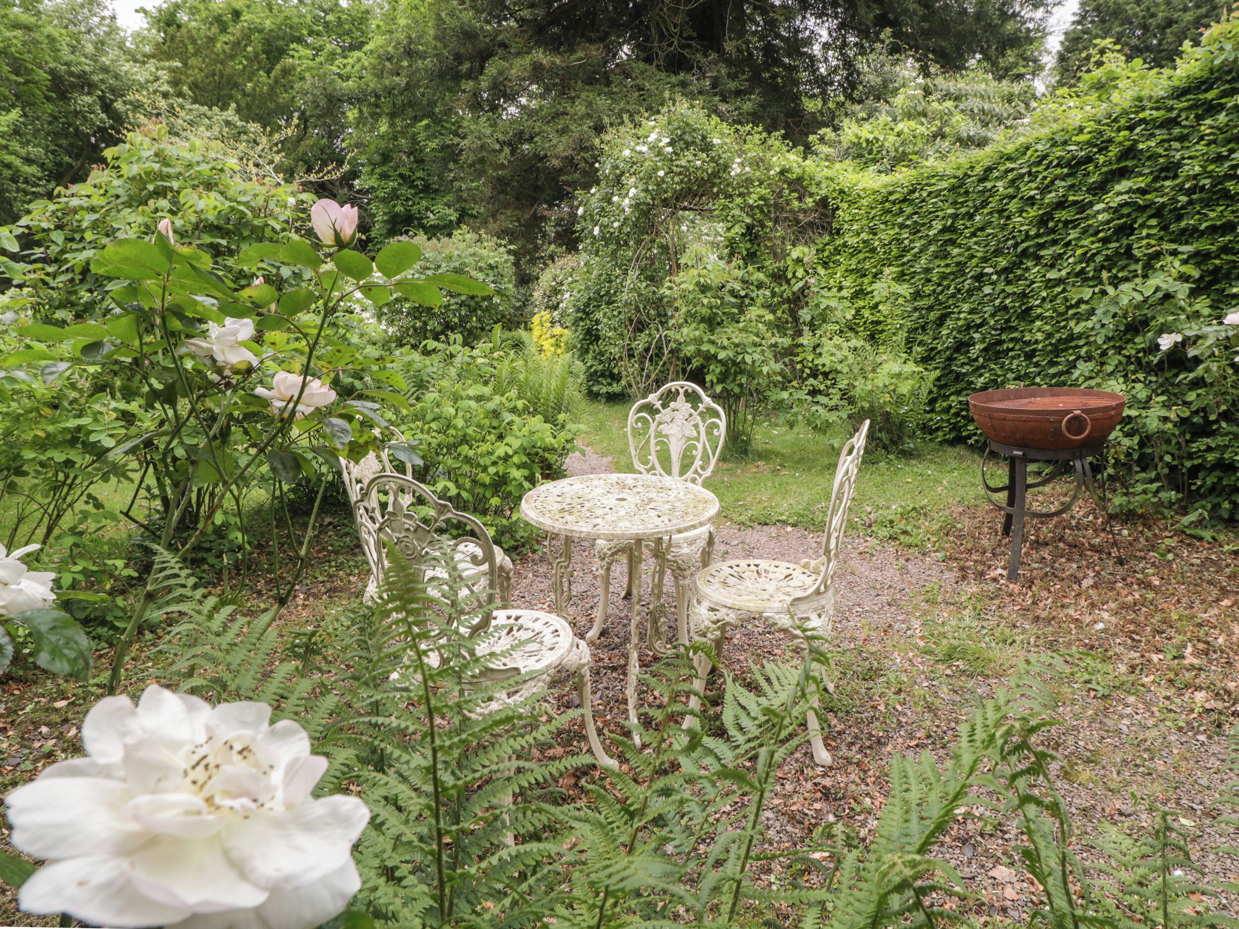 Un jardin avec une table et des chaises en métal, entouré d’une végétation luxuriante et de plantes en fleurs.