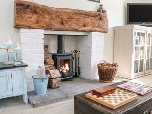 A cozy room with a wood-burning stove, a checkered game board, a basket, and a bookshelf. - 3 Elm Cottage (Minehead)